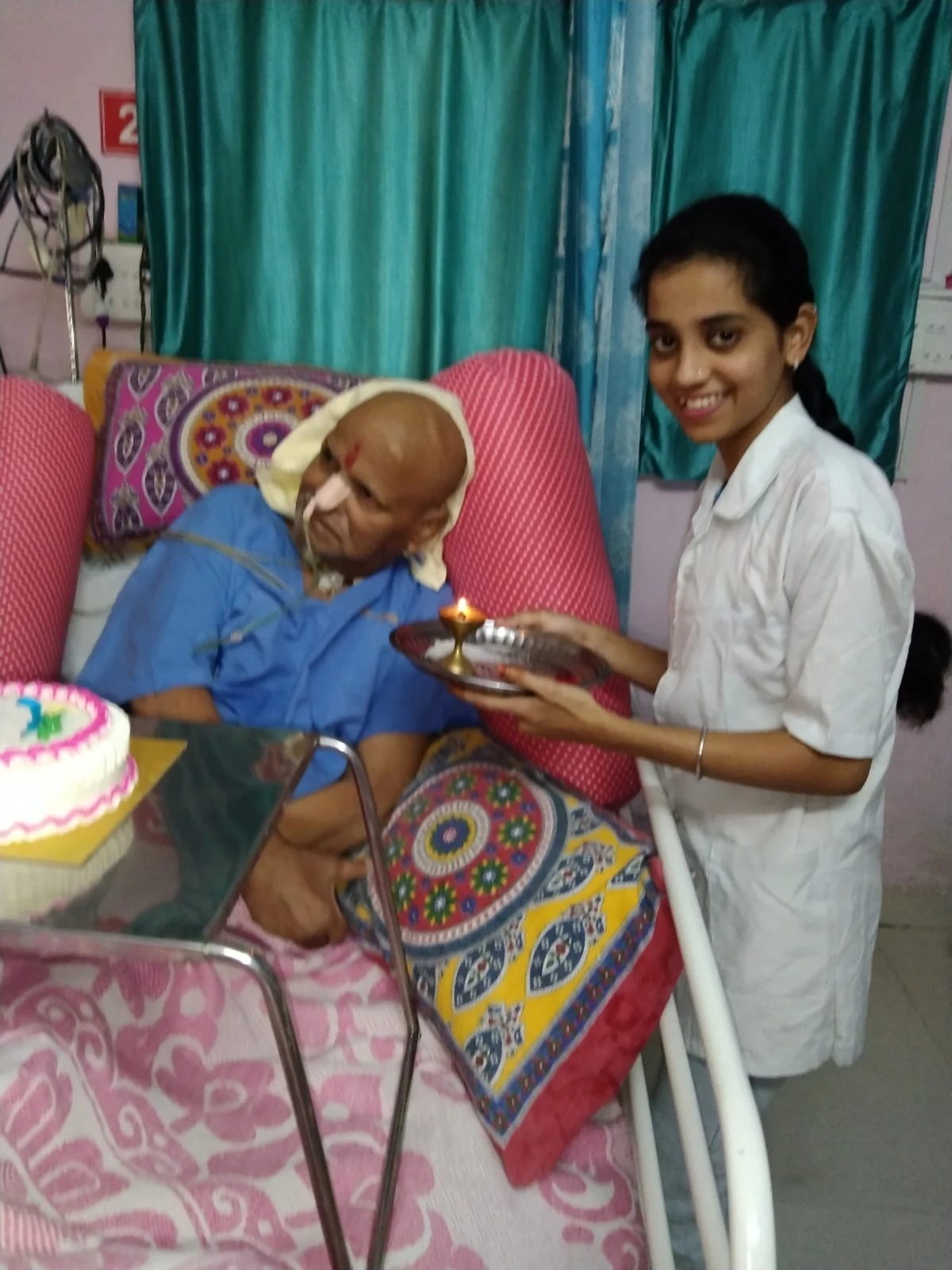 A care worker beside an older man during a bedside celebration at Jeevan Jyoti