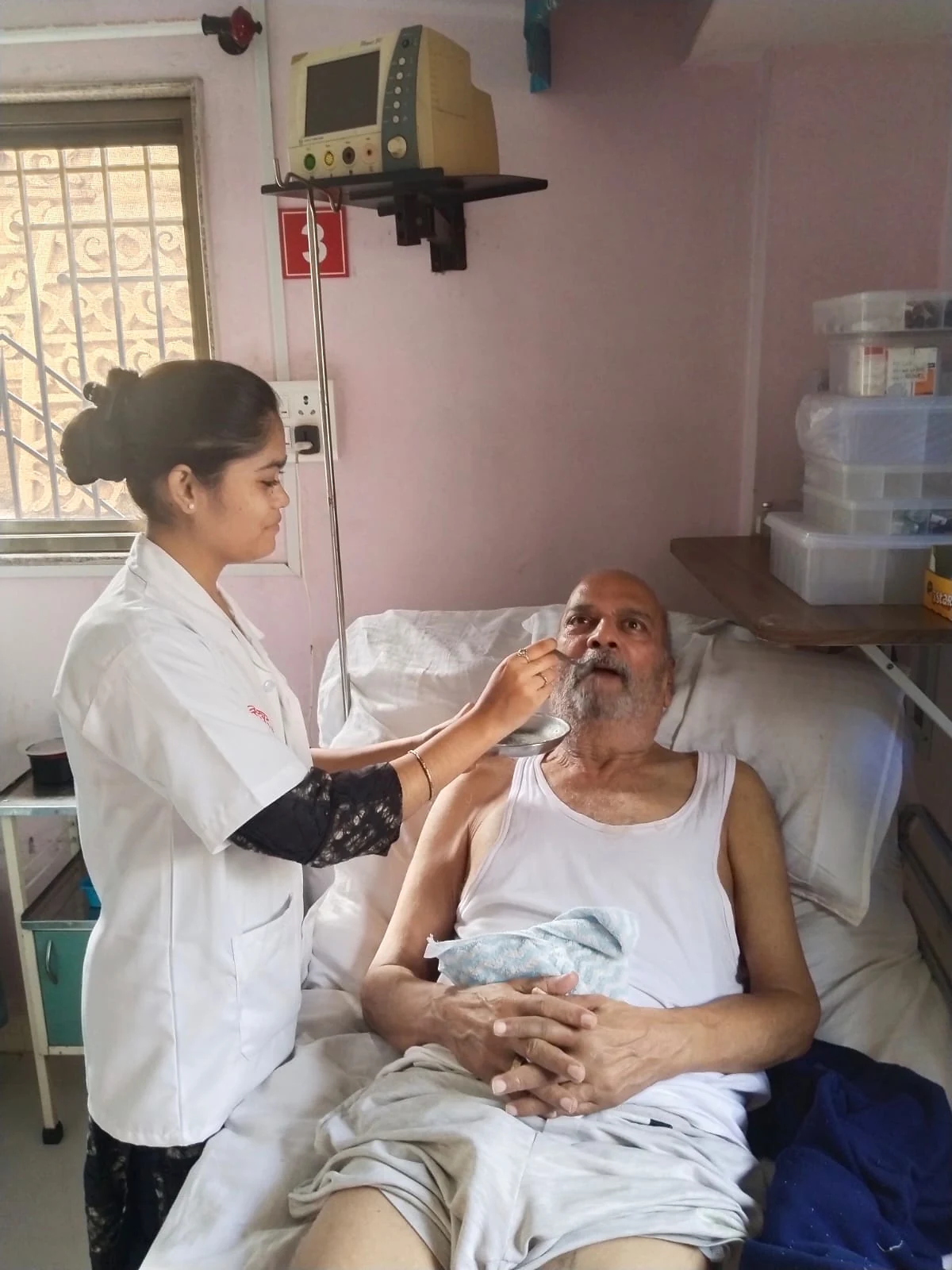 A nurse assisting an older man at his bedside at Jeevan Jyoti