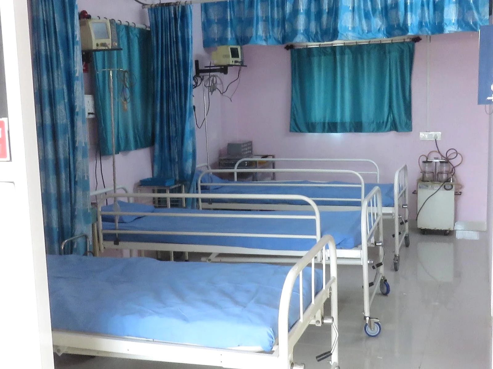 Unoccupied care beds with blue linen and teal curtains at the centre