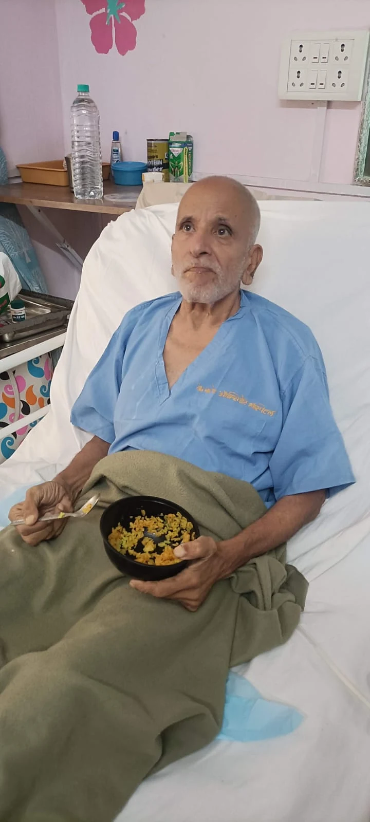 An older man seated in bed with a meal at Jeevan Jyoti